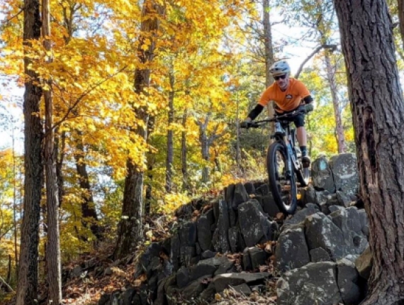 A man mountain biking down rocks in the woods (Instagram@mikc.ferraro)